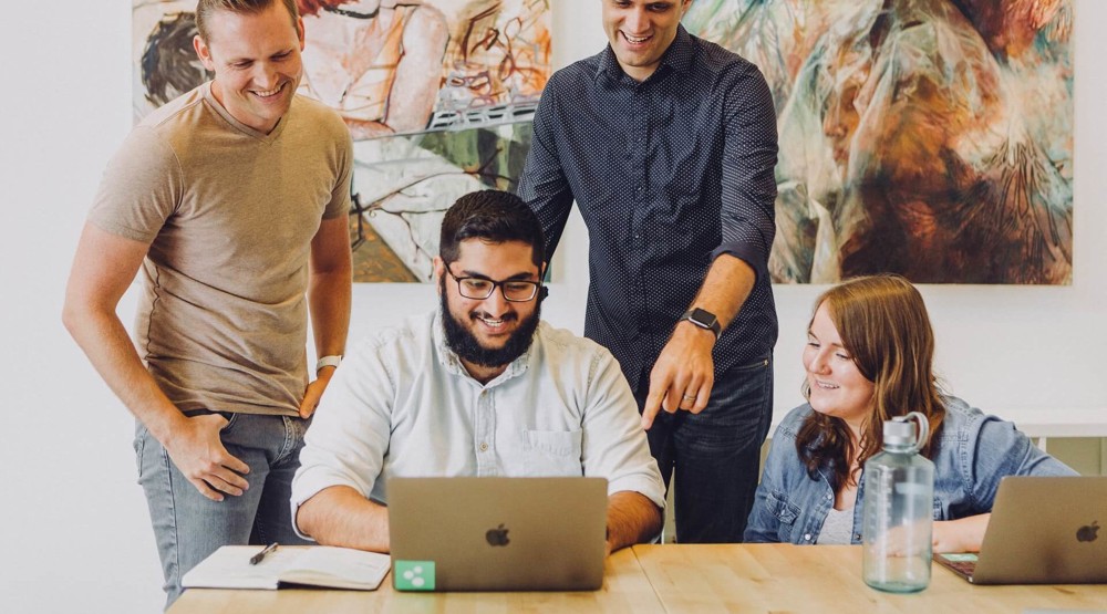 Group of four young businesspeople around a laptop discussing a 1800 phone number