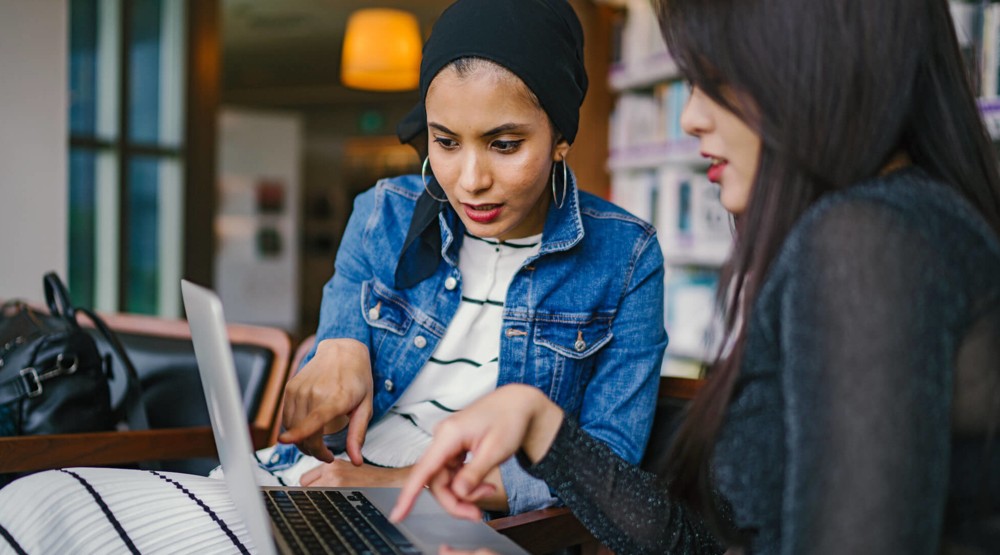 Two businesswomen at a cafe discussing getting a business 1800 number on their laptop