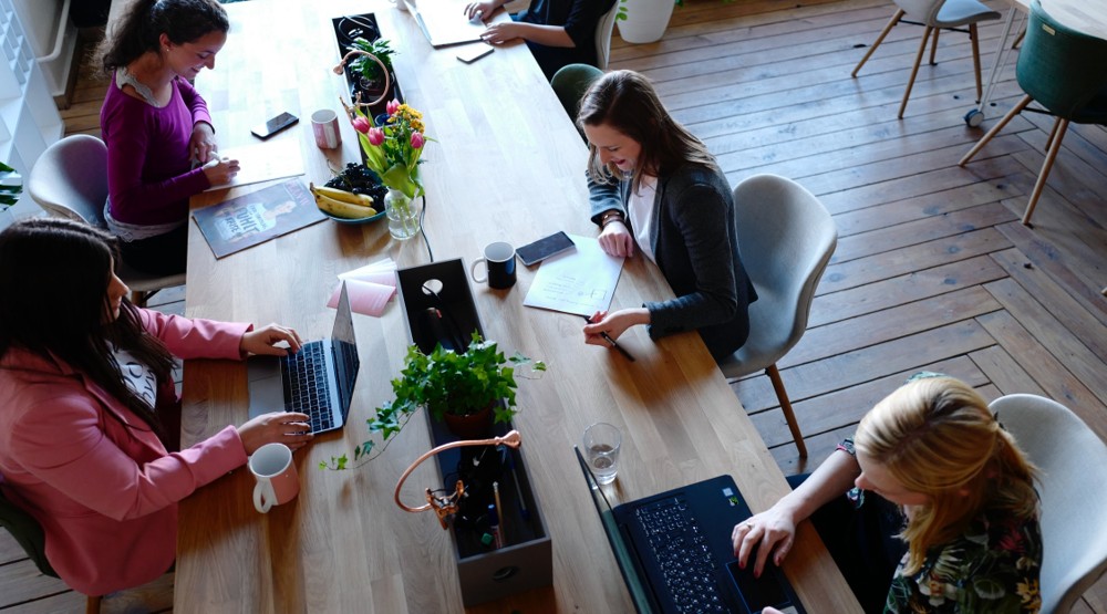 Four businesswomen at a cafe bench discussing buying a 1300 number