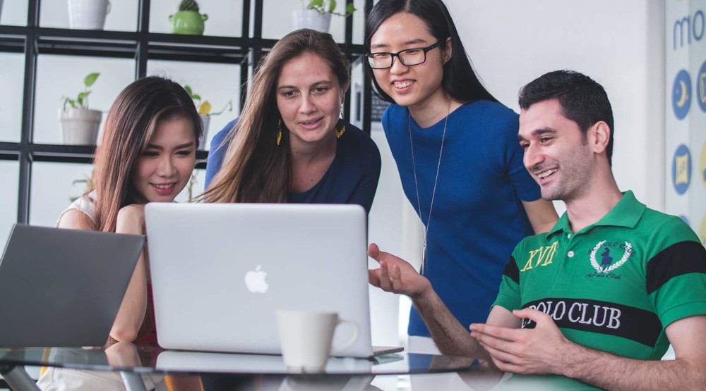 Four young businesspeople around a computer screen discussing buying a 1800 number