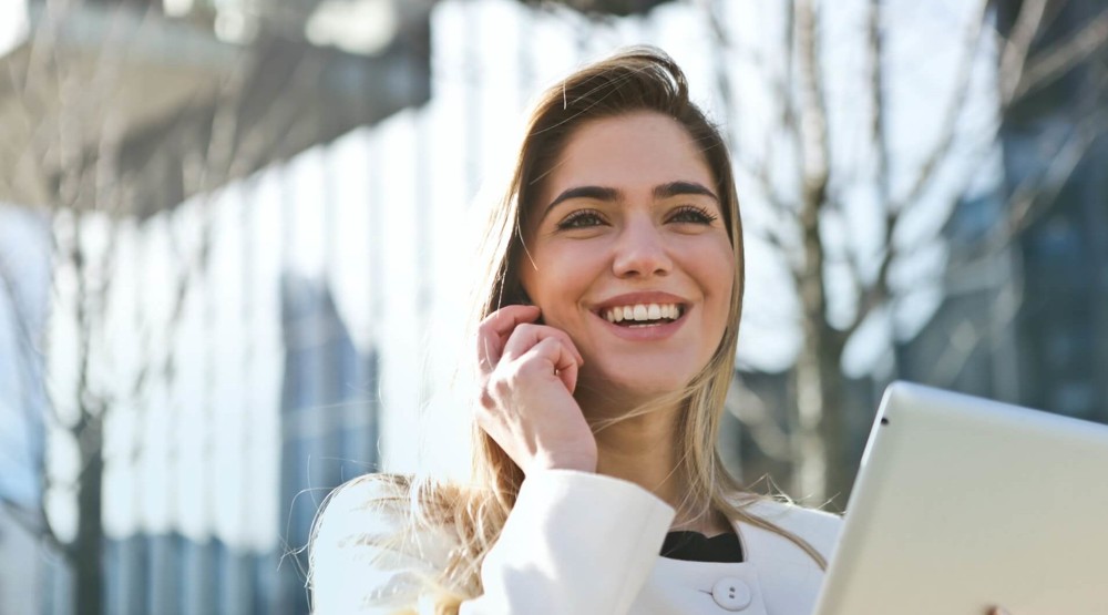 Young businesswoman talking on her mobile phone whilst outside and holding her laptop researching 1300 phone numbers